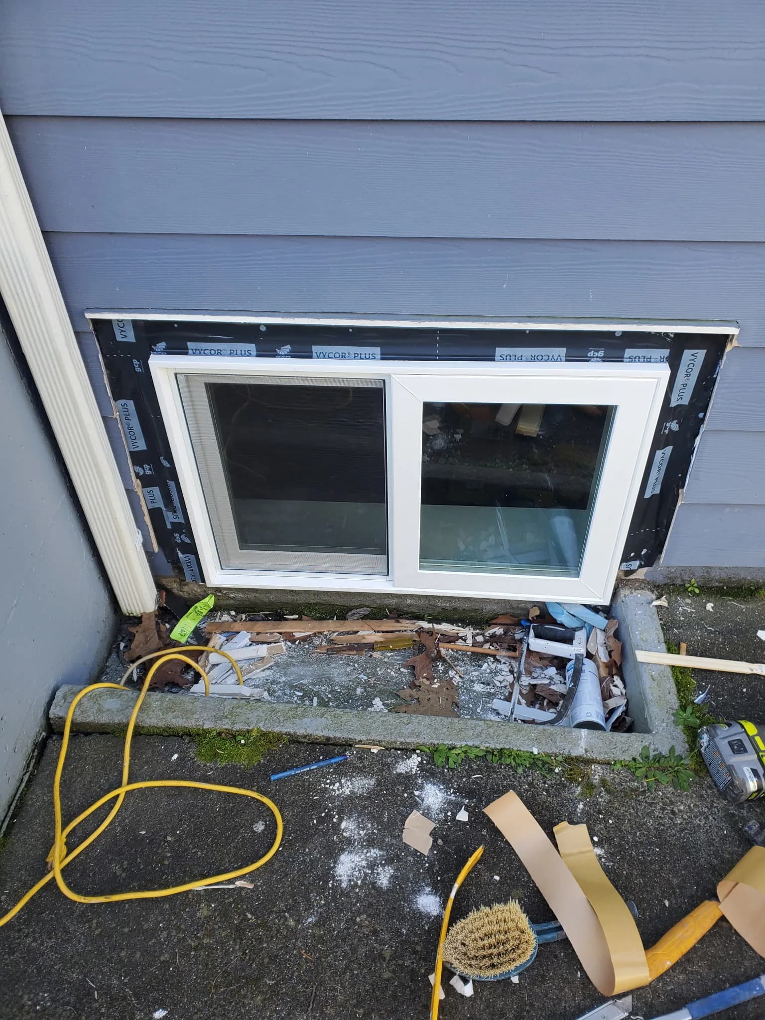 New white-framed lower-level replacement window installed with fresh waterproofing