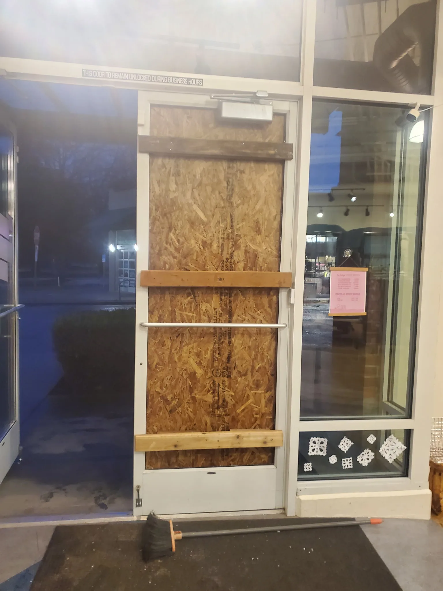 Boarded commercial storefront entry secured after glass damage